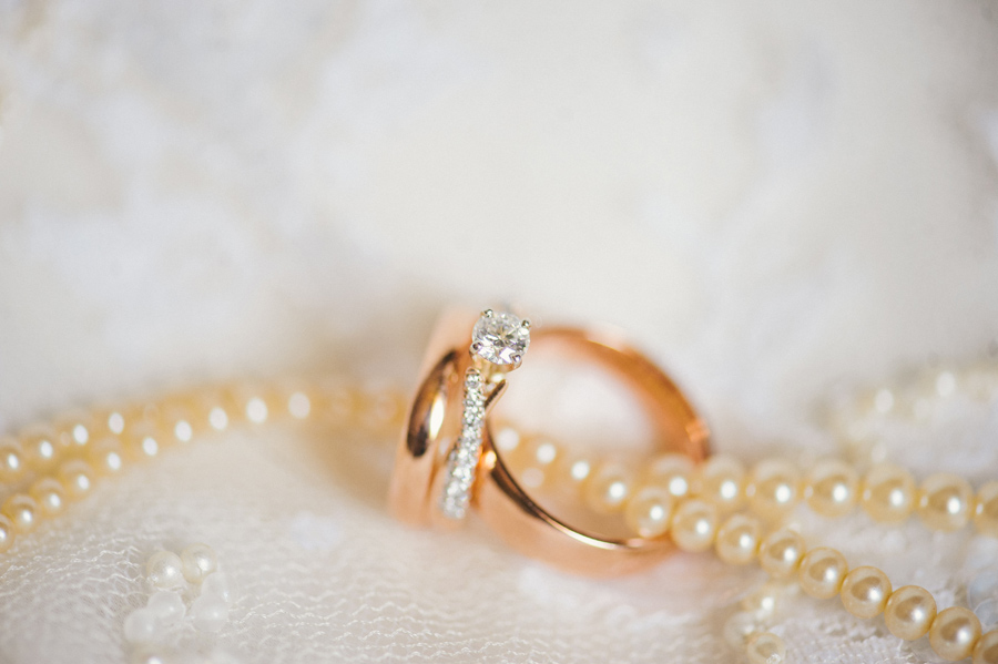 wedding bands and engagement ring laying on lace with ivory pearl necklace