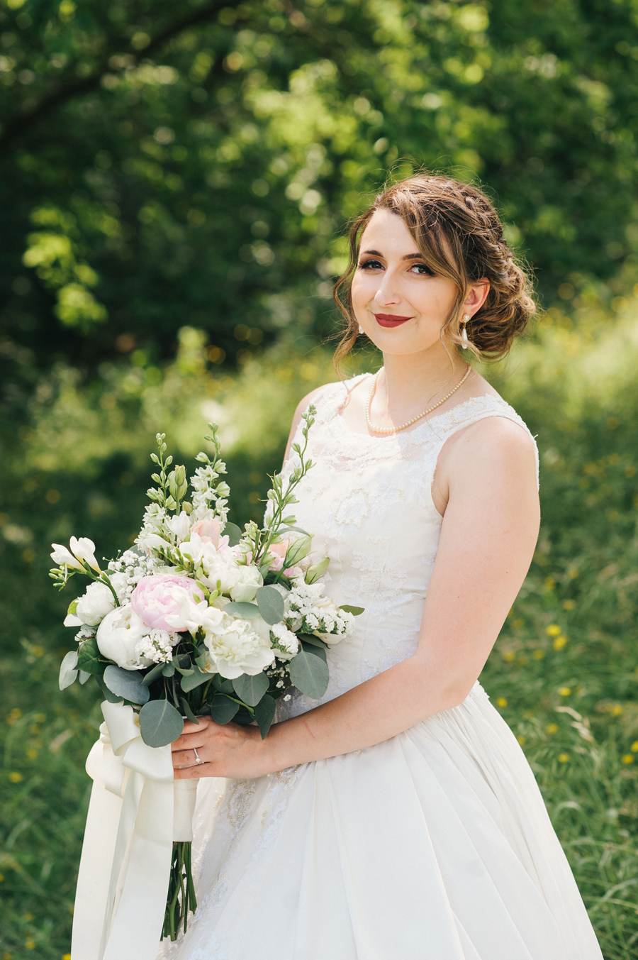 bride smiling and posing with her bouquet of white and light pink flowers