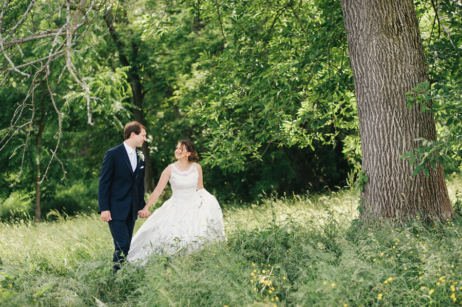 bride and groom strolling hand in hand through a field