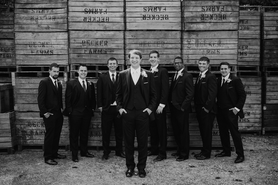 black and white of groom and groomsmen in front of wooden palettes at becker farms