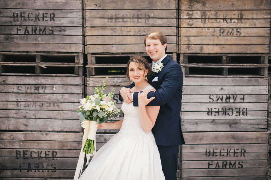 groom wrapping arms around bride in front of wooden crates becker farms