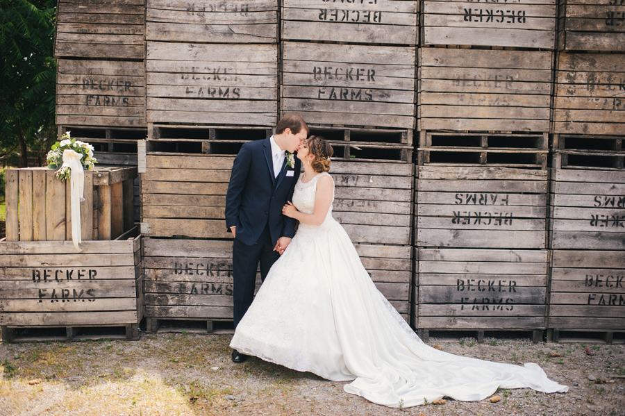 bride and groom kissing in front of wooden crate wall at becker farms