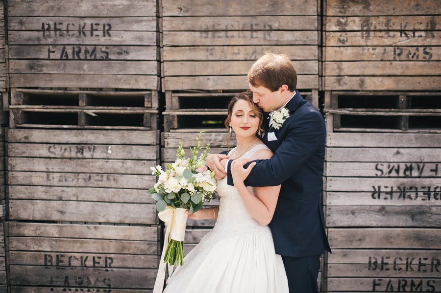 groom kissing brides forehead as he wraps arms around her