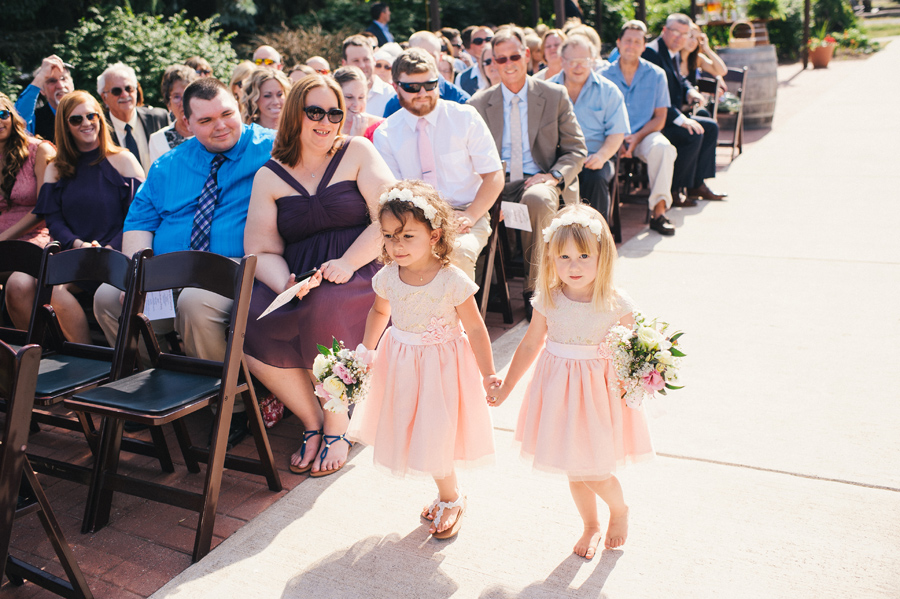 two flowers girls in light pink dresses walking hand in hand down the aisle