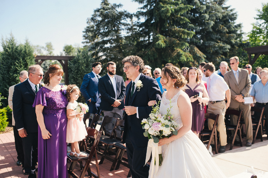 bride and her father smiling as the walk down the aisle