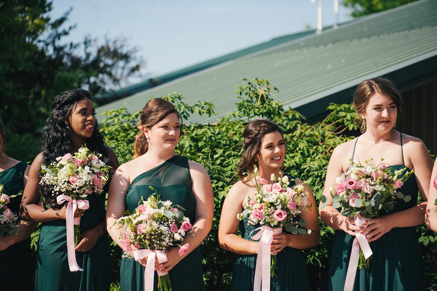 bridesmaids looking on while holding bouquets of white and pink flowers