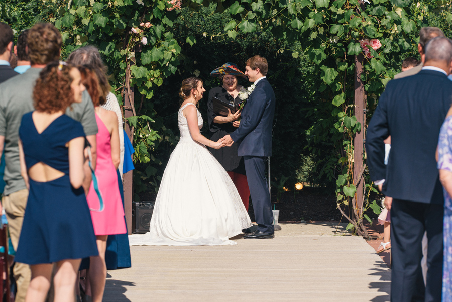 bride and groom facing each other under a grapevine arbor