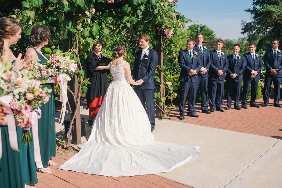 bride and groom holding hands under a grapevine arbor at becker farms