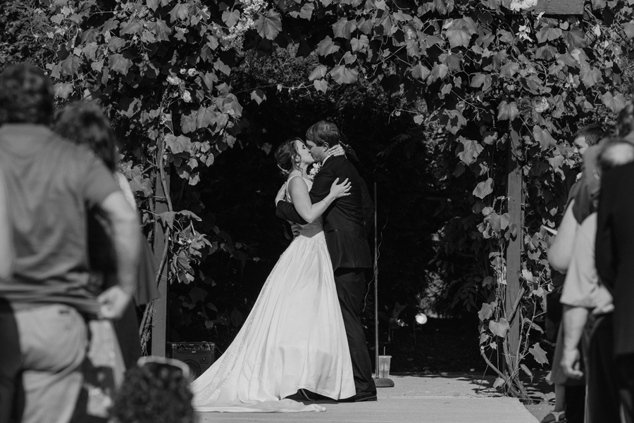 black and white of bride and groom kissing at the end of the wedding ceremony