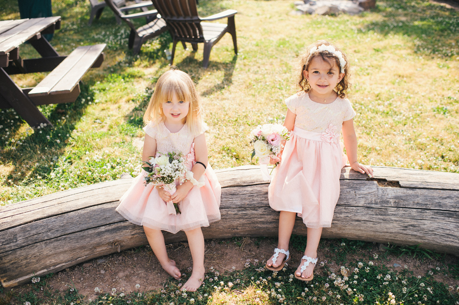 two flower girls sitting on a log with bouquets and light pink dresses