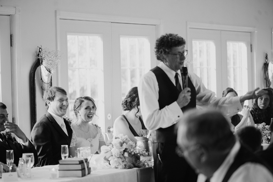 black and white of bride and groom laughing during father of the bride's speech