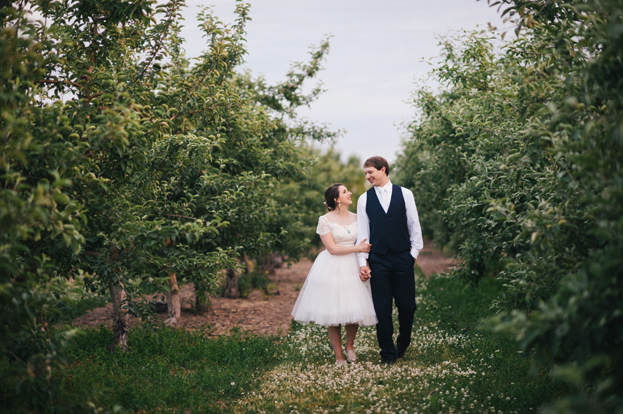 bride and groom walking between rows of apple trees at becker farms