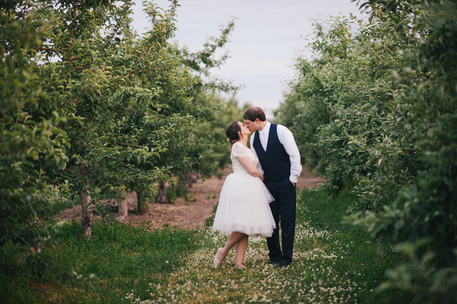 bride and groom kissing in center of apple orchard