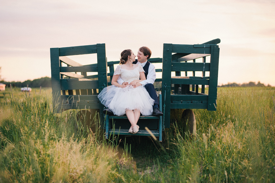 bride and groom sitting on wooden trailer in a field