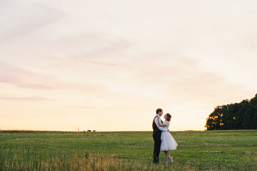 bride and groom gazing at each other in a field at sunset