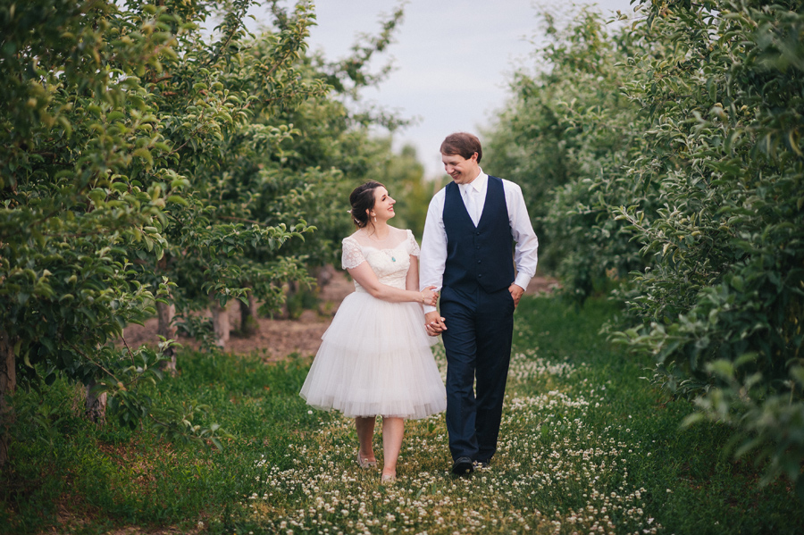 bride and groom strolling hand in hand through apple trees