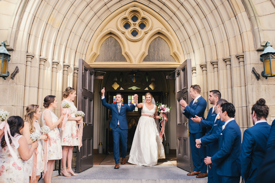 bride and groom exiting the church to cheers of the wedding party