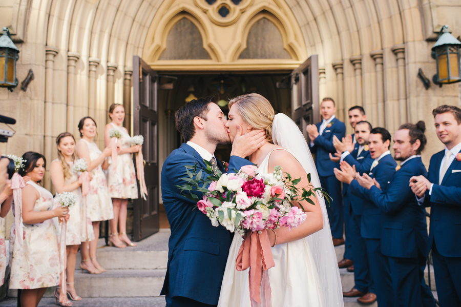 bride and groom kissing in front of st joseph cathedral as wedding party cheers