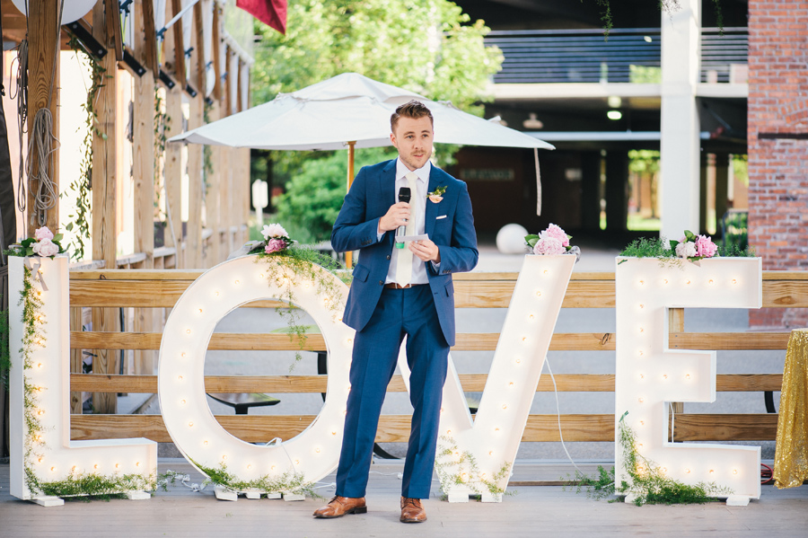 best man delivering his speech in front of giant love marquee letters