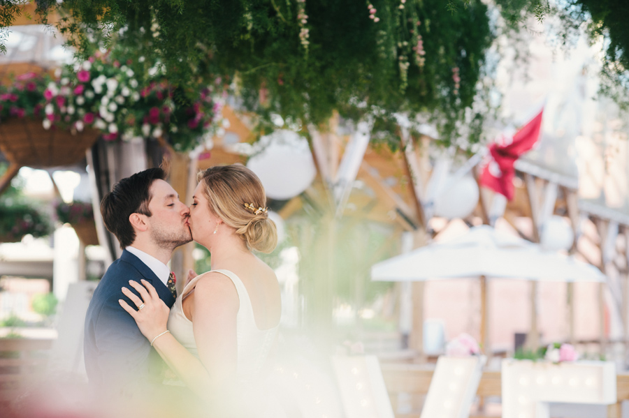 bride and groom kissing underneath the greenery chandelier 