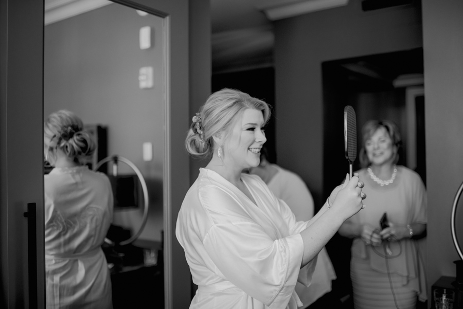 black and white of bride looking at her updo in the mirror