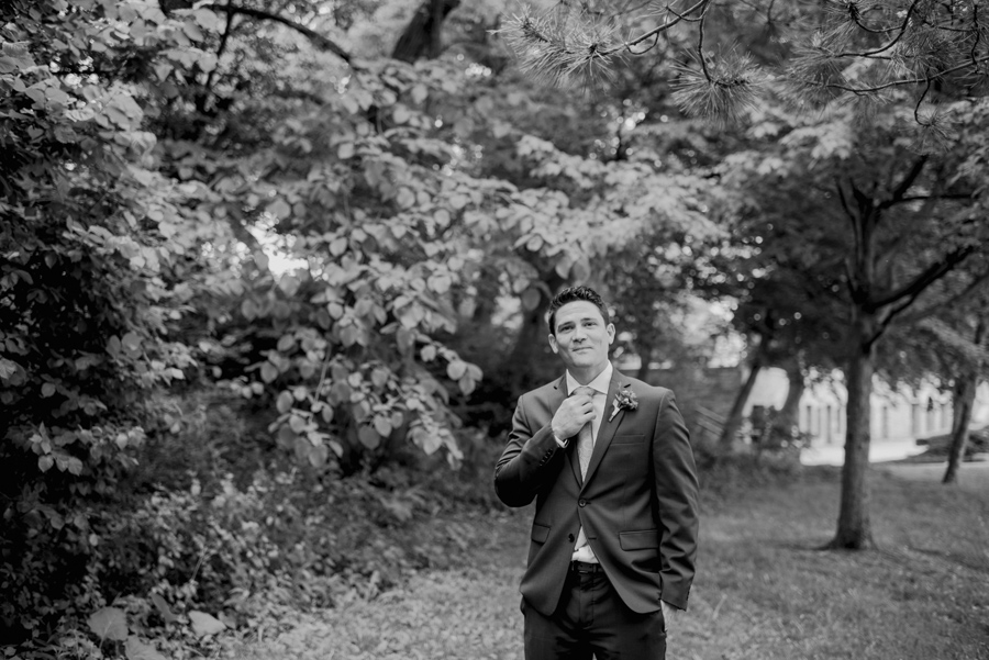 black and white portrait of groom adjusting his tie in the park