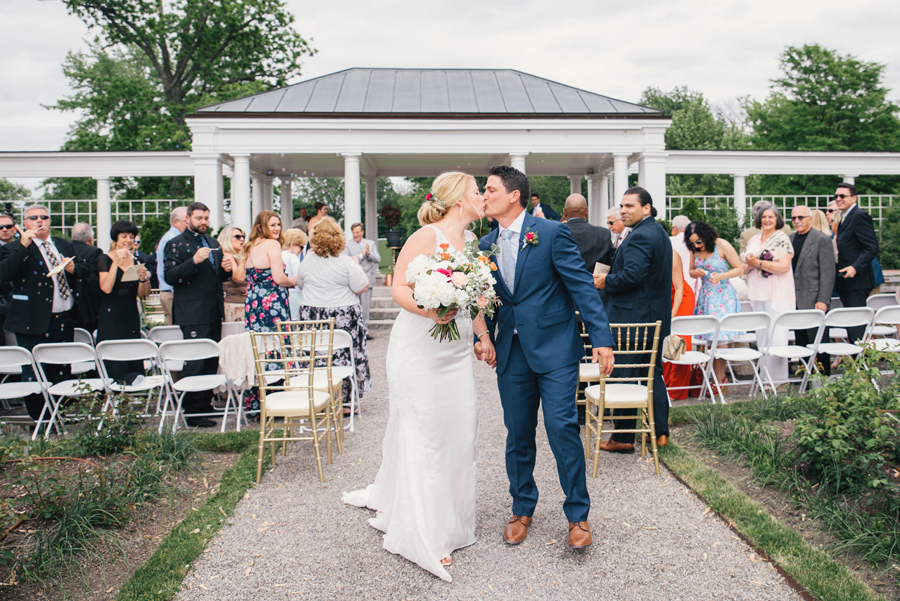 bride and groom kissing at the end of the aisle at delaware park rose garden