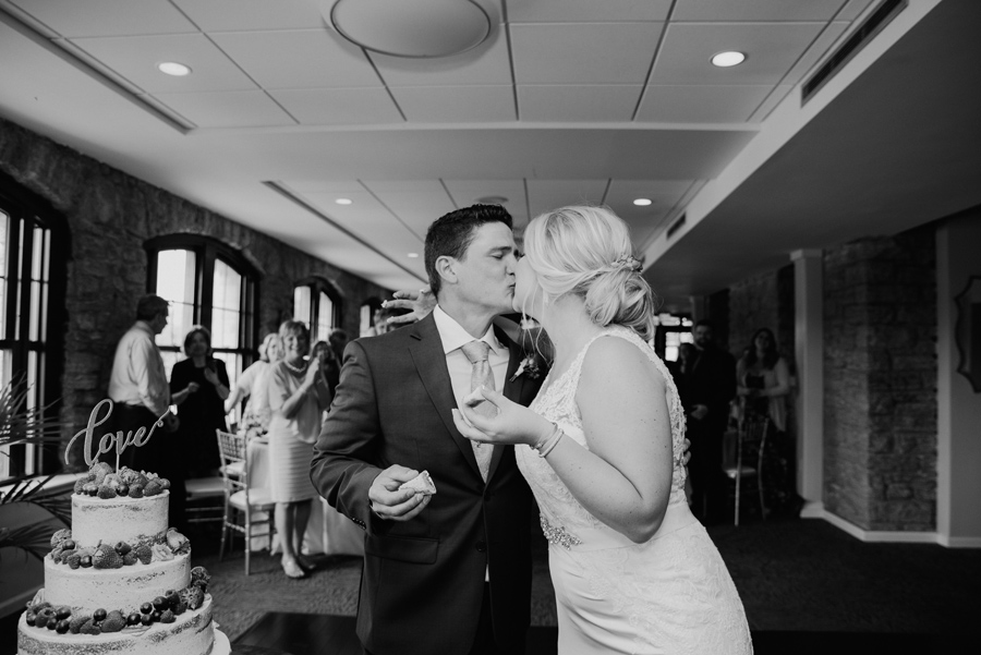 black and white of bride and groom kissing in front of cake