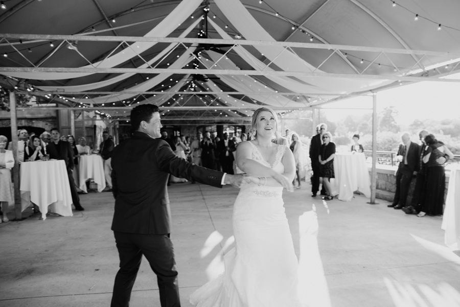 black and white of groom twirling bride during first dance