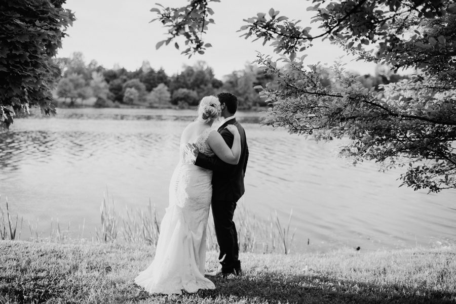 black and white of bride and groom hugging and gazing at the lake together