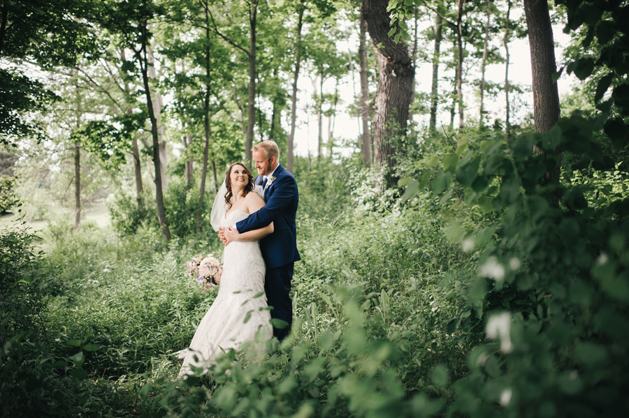 bride and groom standing together in a wooded area