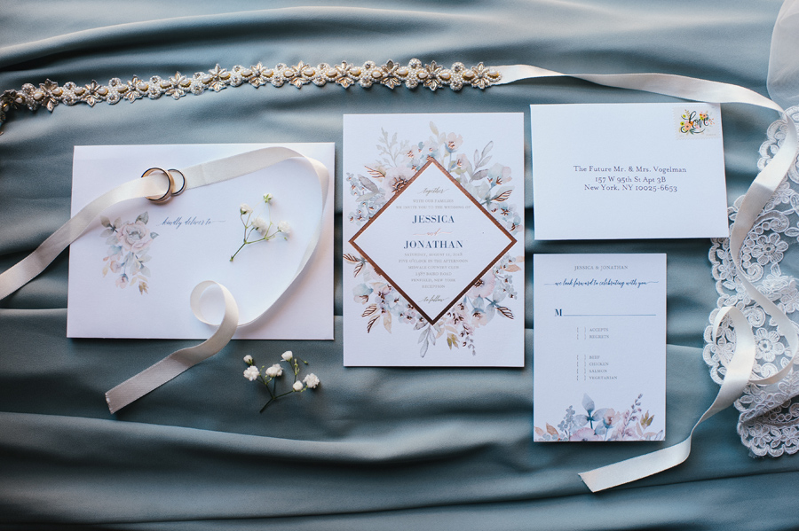 wedding invitation suite with jeweled bridal belt, ribbon and wedding bands on blue satin background
