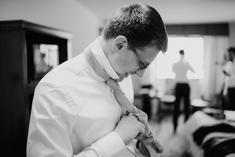 black and white of groom adjusting his tie on wedding morning