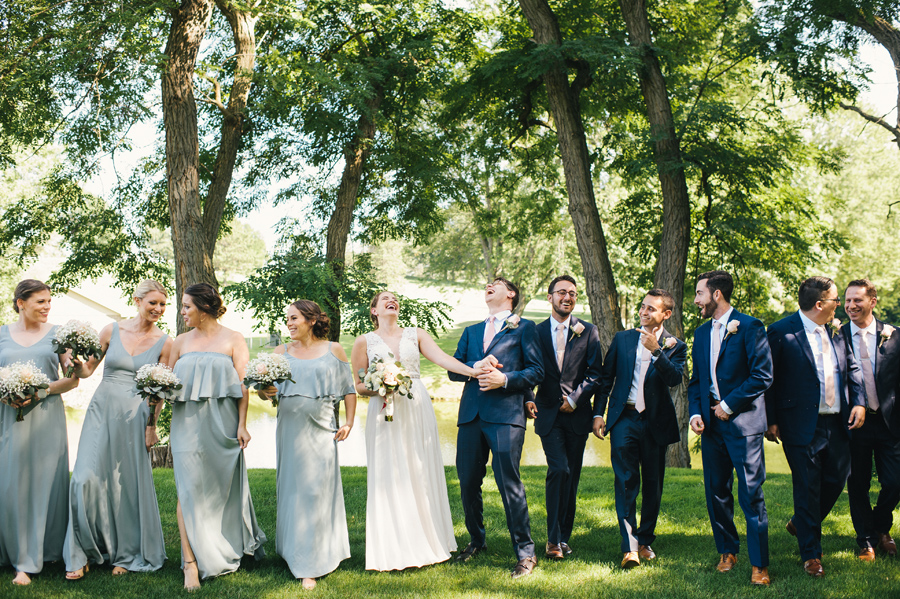 bride and groom throwing their heads back in laughter while they walk with the wedding party towards the camera