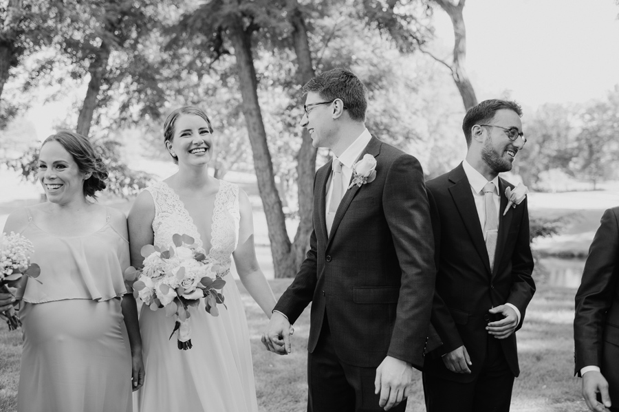 black and white of bride and groom holding hands and smiling while casually hanging out with wedding party