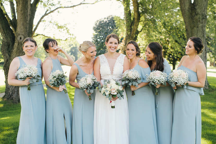 bride and bridesmaids laughing together in a park while posing for the camera