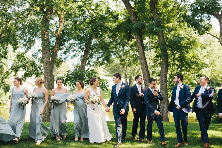 full length of entire wedding party laughing together and walking towards camera in the park