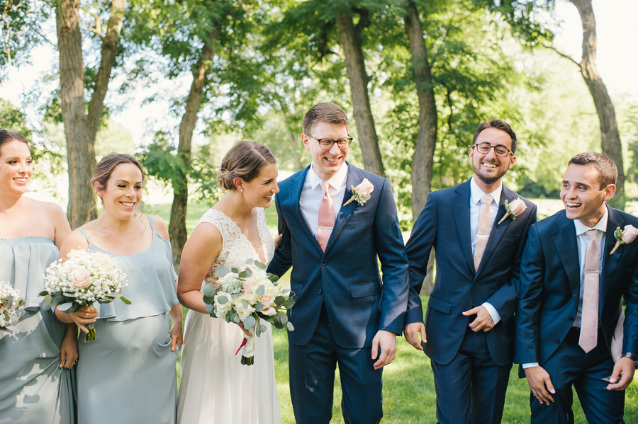 bride and groom laughing with several wedding party members at the park during portraits