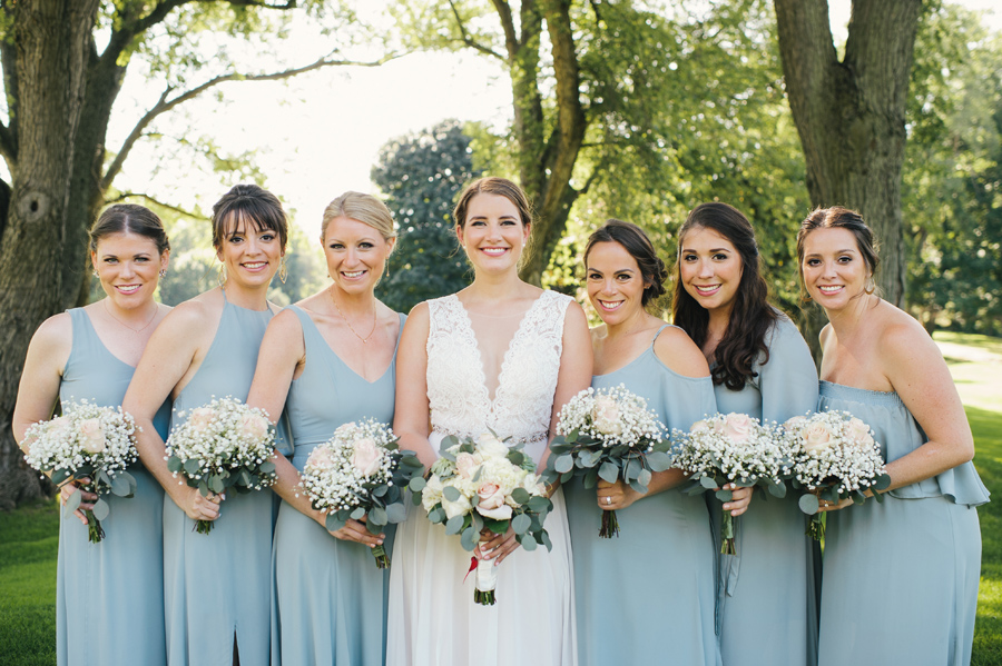 close up of bridal party smiling for the camera with their bouquets of blush roses and baby's breath