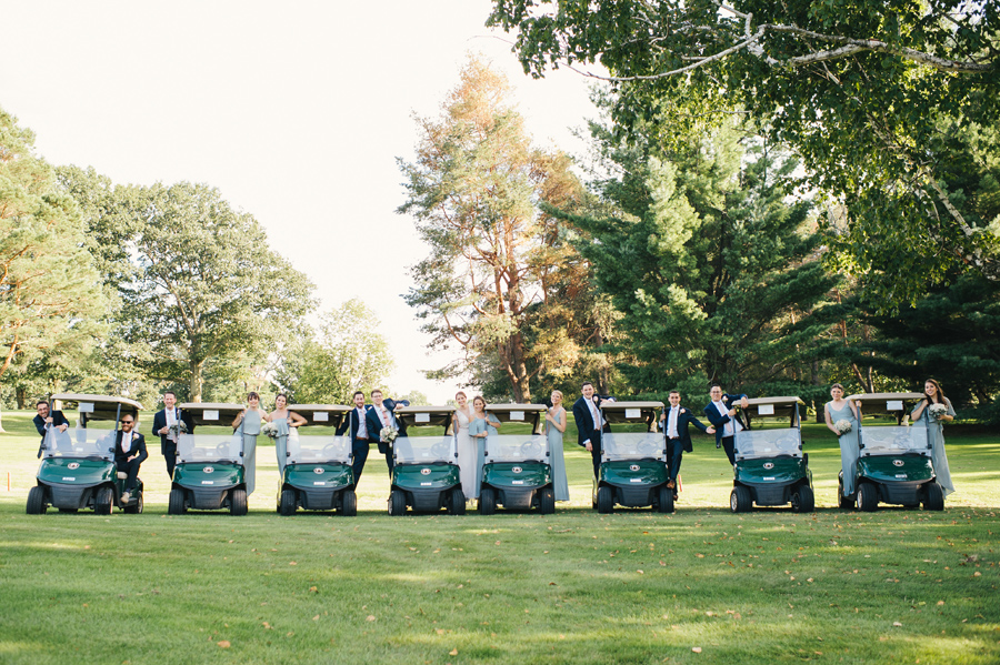 8 golf carts lined up with wedding party members leaning out of the sides