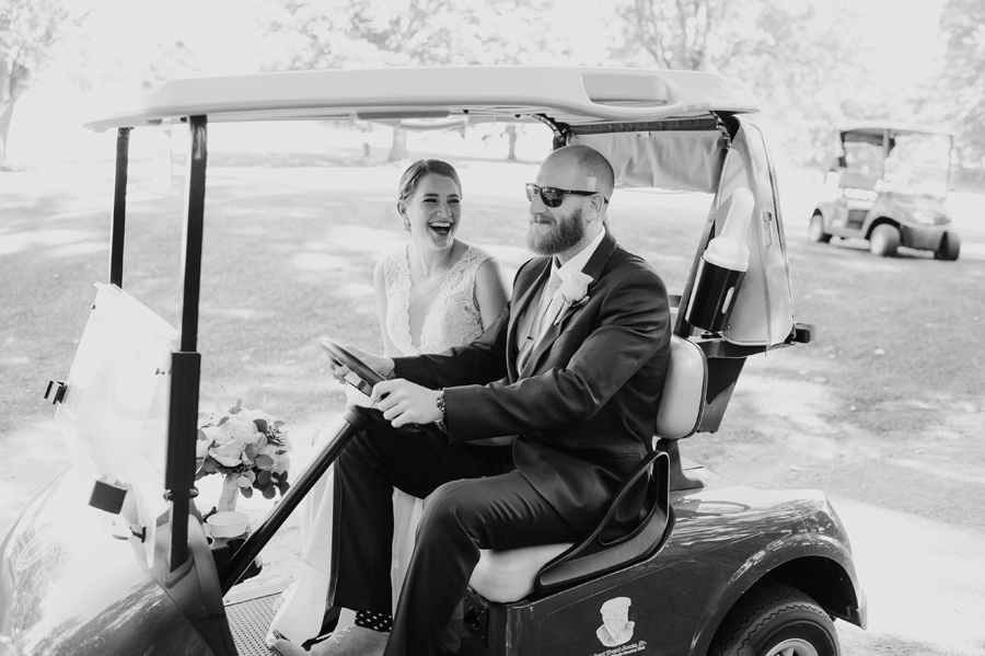 black and white of bride laughing while her brother drives her in a golf cart