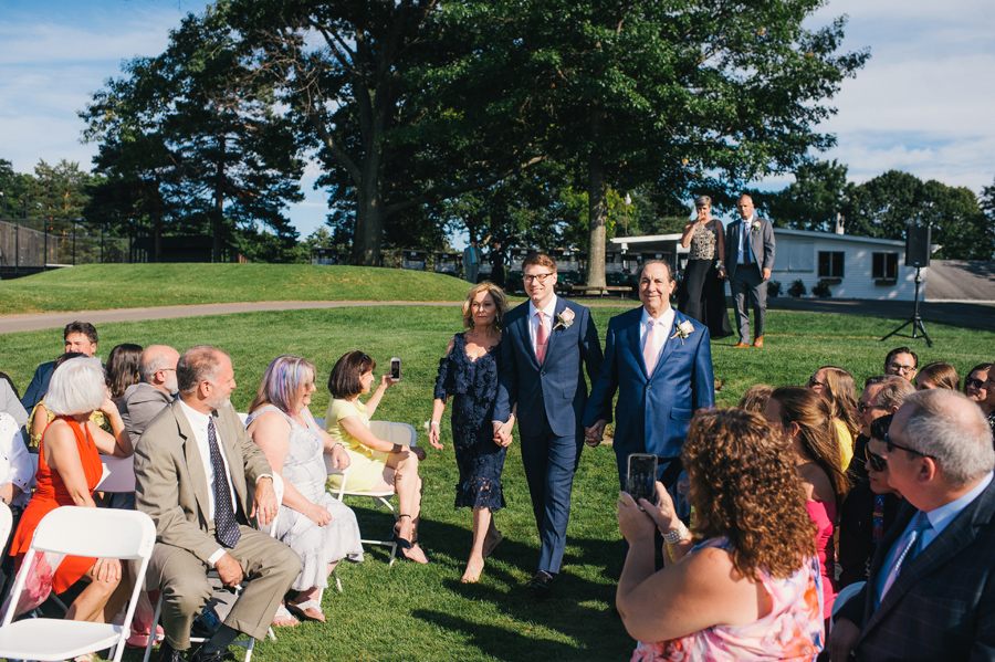 groom being escorted down the aisle by his parents