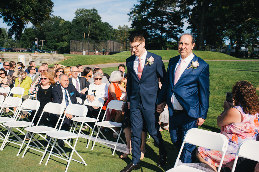 groom's parents walking him down the aisle at the outdoor golf course ceremony