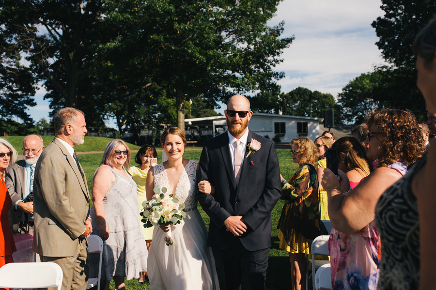 bride's brother escorting her down the aisle while she smiles