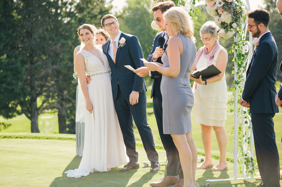 bride and groom smiling with arms around each other during a ceremony reading from family members