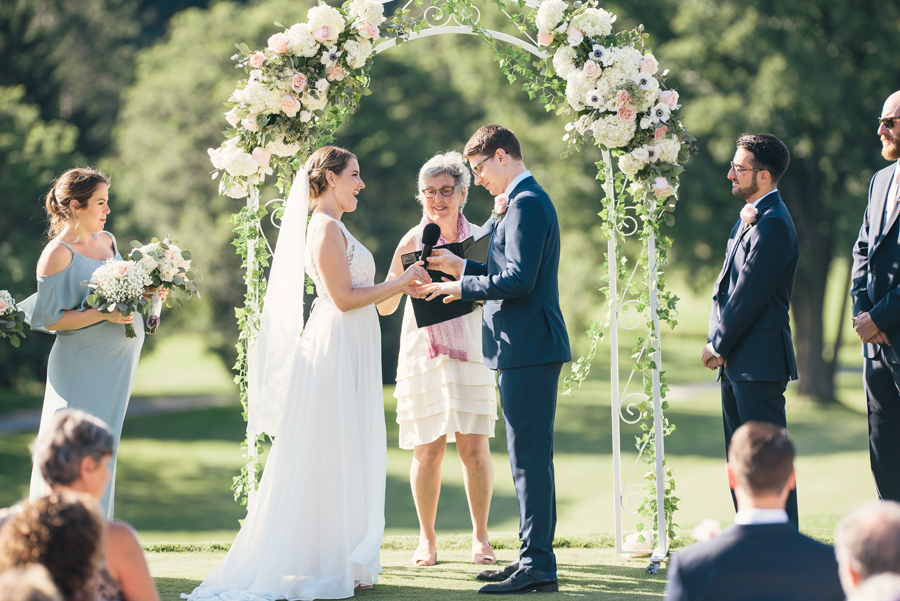 bride laughing while trying to push wedding band onto groom's finger