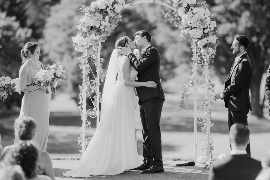 black and white shot of bride and groom's i do kiss at golf course wedding ceremony