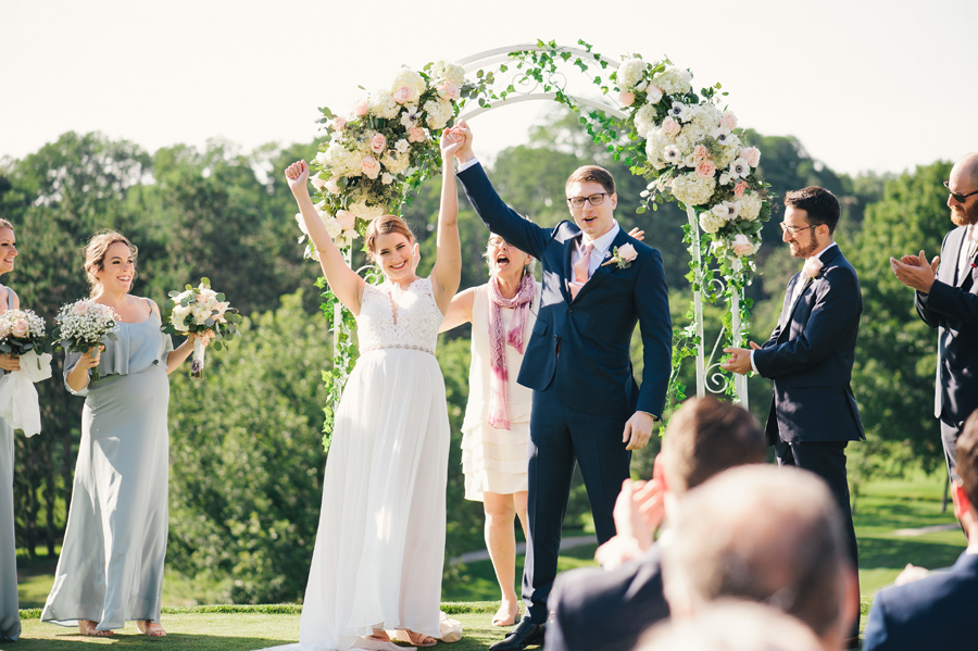 bride and groom facing their guests with arms raised as they're announced as officially married