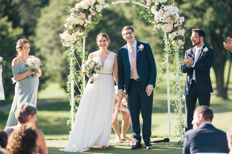 bride and groom smiling at their guests who are clapping for them at the end of their wedding ceremony