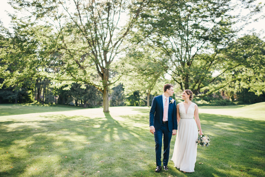 bride and groom strolling together across the green grounds of the country club